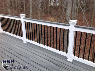 Composite deck using Trex Transcend Island Mist cap railing, white vinyl railing, and square black aluminum balusters.